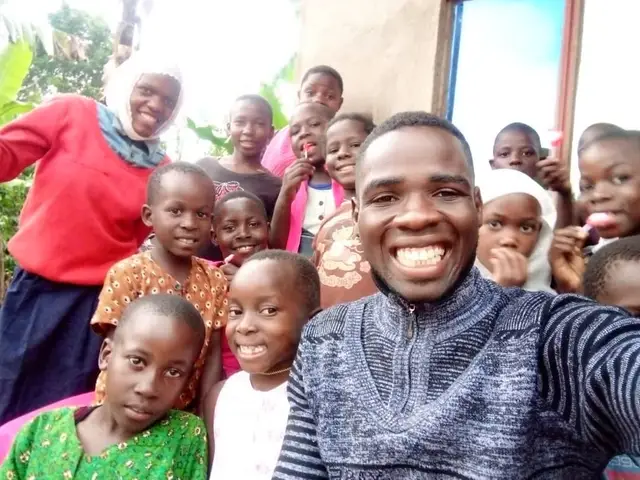 A caregiver taking a selfie with a dozen children, several holding toothbrushes