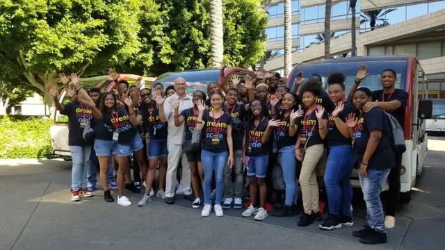 Students in Dream Hustle Code shirts waving beside studio tour trams